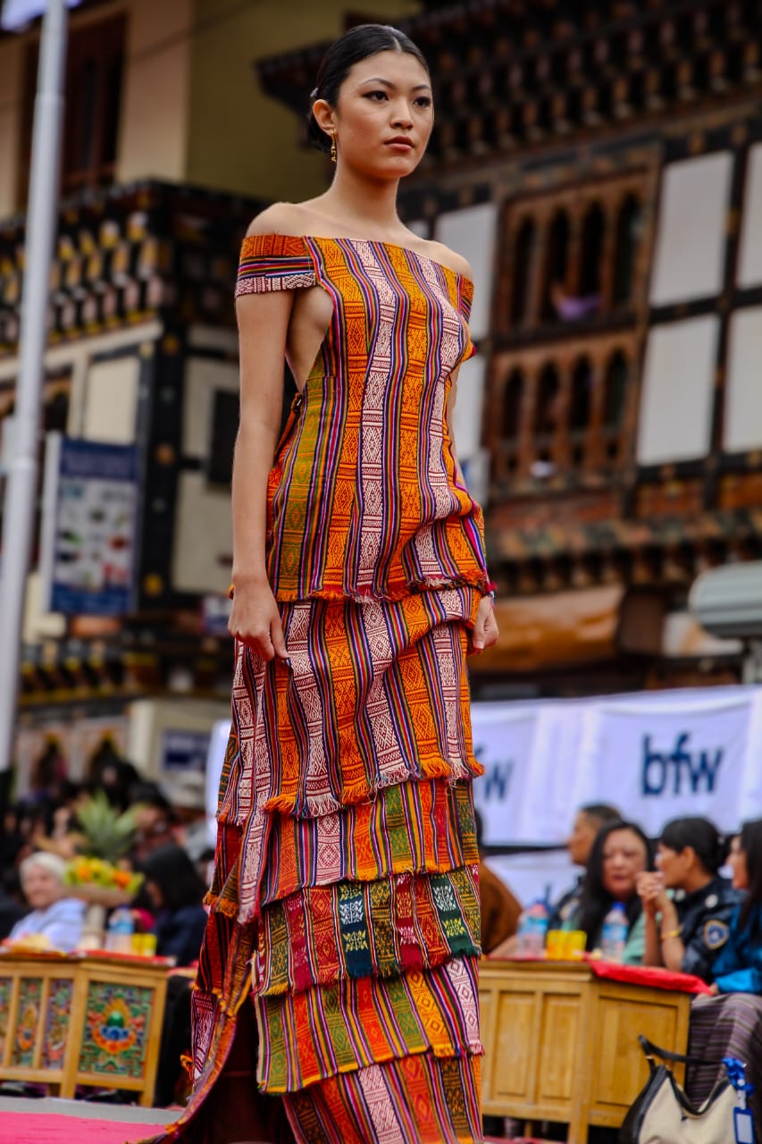 A dress created entirely from waste materials gathered from a Bhutanese tailor - offcuts of gho and kira fabrics. Each piece has been reimagined into a flowing silhouette, celebrating the artistry and resilience of Bhutanese textiles.